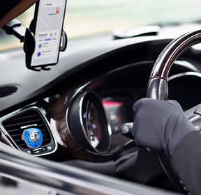 A mobile phone showing navigation on the screen and hands on a car steering wheel